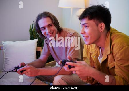 Joyeux jeunes hommes enthousiastes jouant à des jeux vidéo à la maison Banque D'Images