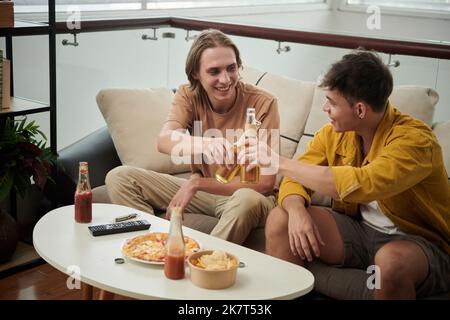 Des amis souriants buvant des bières et mangeant des pizzas à la maison Banque D'Images