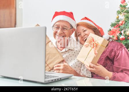 Un couple latin senior a accueilli ses proches par appel vidéo à Noël, leur montrant leurs cadeaux. Concepts: La joie de partager pendant les vacances, le Banque D'Images