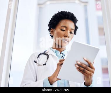 En utilisant des ressources médicales en ligne. Prise de vue en contre-plongée d'une jeune femme médecin attirante utilisant sa tablette au bureau. Banque D'Images