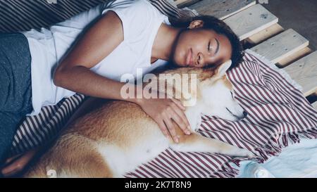 Magnifique Africain américain adolescent et adorable chien d'animal de compagnie dorment ensemble sur un lit en bois, fille porte confortable pyjama et l'animal de garde. Concept de repos et d'amitié. Banque D'Images