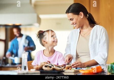 Nous faisons une excellente équipe dans et hors de la cuisine. une petite fille aidant sa mère à hacher des légumes à la maison. Banque D'Images