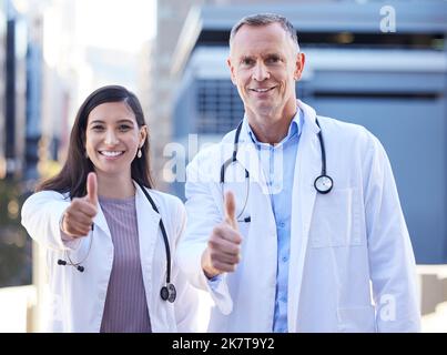 Humble et disposé à se battre. Portrait de deux médecins montrant les pouces dehors dans la ville. Banque D'Images