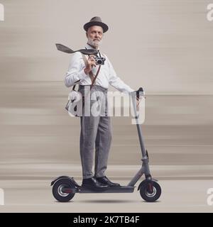 Homme de style vintage portant une valise et portant un scooter électrique, il est un voyageur et un photographe Banque D'Images