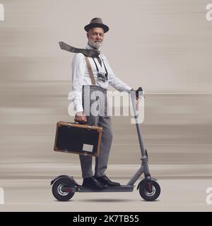 Homme de style vintage portant une valise et portant un scooter électrique, il est un voyageur et un photographe Banque D'Images