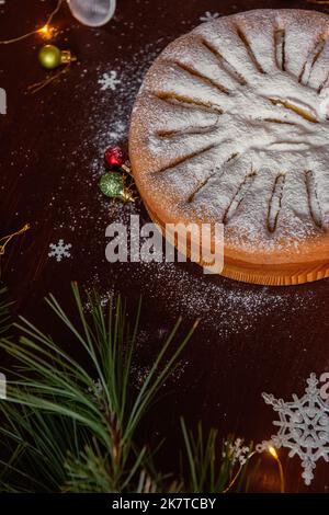 Sur une table brune en bois se trouve une pomme charlotte arrosée de sucre en poudre. Vue de dessus de la pose à plat. La branche verte d'un pin se trouve à côté de la tarte, un Banque D'Images