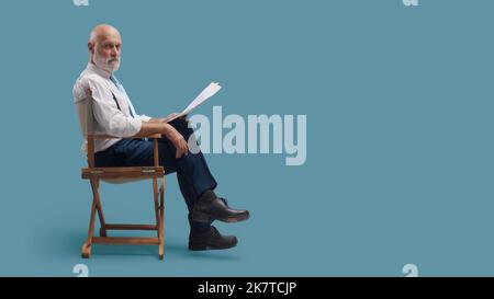 Réalisateur professionnel assis sur la chaise du réalisateur et tenant un scénario, il regarde la caméra Banque D'Images