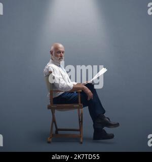 Réalisateur professionnel assis sur la chaise du réalisateur et tenant un scénario, il regarde la caméra Banque D'Images