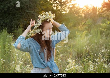 Belle jeune femme tenant le bouquet de fleurs sauvages et marchant dans le champ de fleurs au coucher du soleil. Banque D'Images