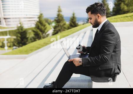 Un homme en costume est assis sur les marches d'un escalier de ville avec un ordinateur portable. Pause-travail. Extérieur. Style de vie professionnel Banque D'Images
