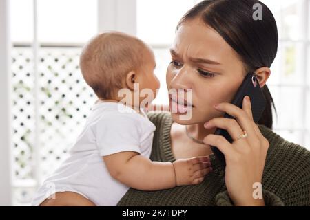 J'ai besoin d'un baby sitter. une jeune femme utilisant un smartphone tout en transportant son bébé à la maison. Banque D'Images