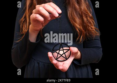 Une femme portant une robe noire démontre un grand collier de pentagramme. Banque D'Images