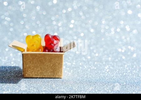 Gros plan de deux bonbons à l'ours en peluche placés dans une boîte d'expédition miniature isolée sur un fond étincelant avec espace de copie. Banque D'Images