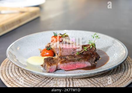 Le steak de bœuf moyen rare était grillé et frit avec des champignons en tranches et une mini tomate sur un plat blanc, prêt à servir et à manger. Banque D'Images