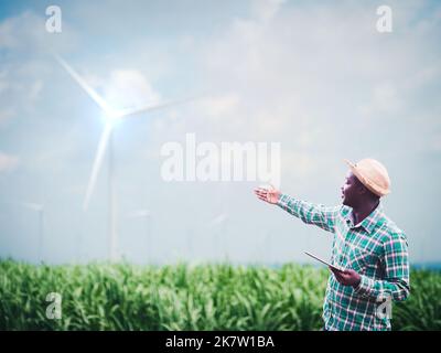 Agriculteur africain debout et tenant une tablette numérique sur la ferme avec l'éolienne en arrière-plan.concept de développement de ressources de durabilité d'énergie verte Banque D'Images