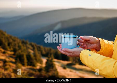 Femme tenant une tasse de voyage avec une boisson chaude. Rafraîchissements pendant la randonnée en montagne. Détente à l'extérieur Banque D'Images