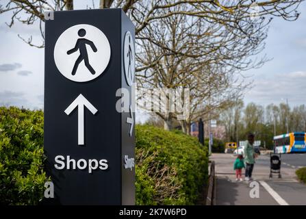 Grand poteau de signalisation directionnel avec flèche et icône de personne marchant pointant le long du chemin vers la zone de vente au détail. Banque D'Images
