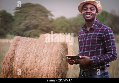 Agriculteur africain dans le champ de blé après la récolte examinant la balle, roulé de paille avec la tablette en main Banque D'Images