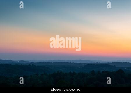 Les couches de colline se séparent par la brume et la lueur vive dans le ciel au-dessus de l'horizon au crépuscule, paysage rural vallonné avec la dernière lumière sur ciel clair Banque D'Images