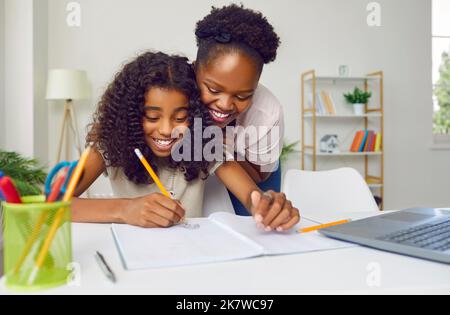 Bonne mère à la peau sombre en regardant sa fille adolescente écrire et dessiner à la maison. Banque D'Images