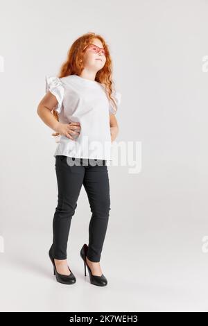 Petit fashionista. Portrait d'une petite fille à tête rouge portant des talons de mère isolée sur fond blanc. Émotions des enfants, expressions du visage Banque D'Images