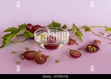 un bol en verre avec de l'huile de pépins de raisin naturel sur fond rose avec une vigne. huile organique. médecine alternative Banque D'Images