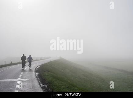 couple sur des balades à vélo dans la brume sur la digue près du rhin en hollande Banque D'Images