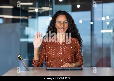 Vue webcam, femme latino-américaine souriante et souriante souriant et regardant la caméra en signe de salut geste, support technique et employé du service à la clientèle, de l'aide en ligne. Banque D'Images