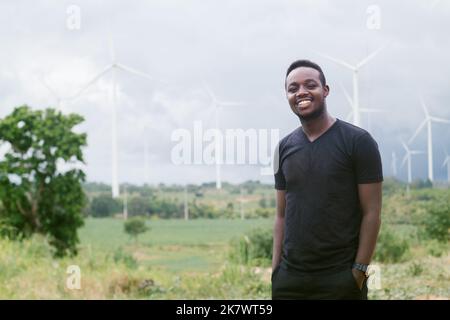 L'homme africain se tient à un moulin à vent qui génère de l'électricité et des énergies renouvelables pour l'agriculture et les moyens de subsistance Banque D'Images