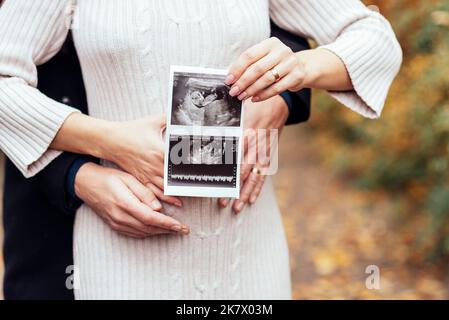 Couple heureux avec la grossesse news holding ultrasound scan de bébé. Femme enceinte et son mari s'attendant l'enfant. La grossesse, maternité concept. Les parents h Banque D'Images