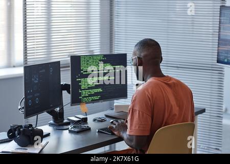 Vue arrière minimale de l'homme afro-américain écrivant le code dans les lignes vertes et utilisant des ordinateurs dans le bureau, l'espace de copie Banque D'Images