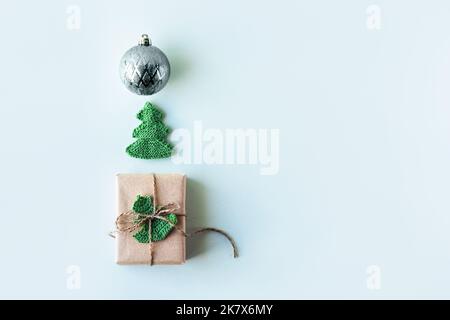 Composition de Noël d'une boîte cadeau en papier gris artisanal décoré d'un sapin de Noël vert tricoté et d'une boule de Noël sur fond vert, le Banque D'Images