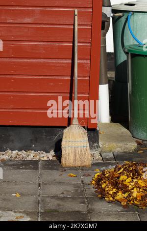 Balai artisanal sur un mur en bois après avoir balayé les feuilles d'automne Banque D'Images