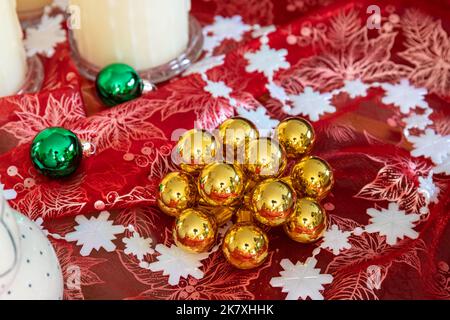 Décorations de Noël boules rondes dorées et vertes sur tissu rouge scintillant avec guirlande blanche en flocons de neige sur la table Banque D'Images