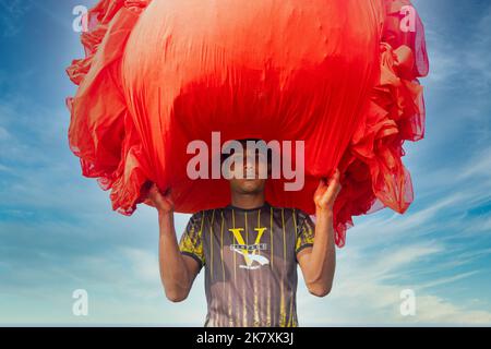 Narsingdi, Dhaka, Bangladesh. 19th octobre 2022. Un waker transporte des tissus pliés alors que des centaines de mètres de tissus rouge vif sont disposés en rangées nettes sur un terrain de Narsingdi. Connus sous le nom de « Lal Shalu » pour les habitants, les longs chiffons rouges sont mis à sécher sous le soleil chaud, ayant été teints avec la couleur rouge vif. L'utilisation de la lumière du soleil pour sécher les tissus réduit les coûts de production car elle est moins chère et plus durable. (Image de crédit : © Joy Saha/ZUMA Press Wire) Banque D'Images