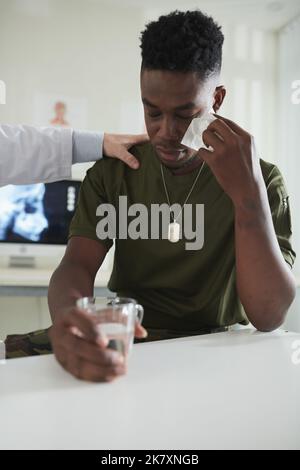 Pleurer un militaire essuyant des larmes et buvant un verre d'eau dans un cabinet médical Banque D'Images