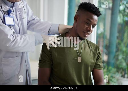 Le jeune soldat ressent une douleur sévère lorsque le médecin palpe son cou et son épaule Banque D'Images