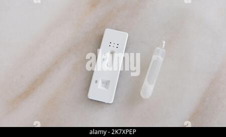 Un kit de test à domicile avec le récipient contenant l'échantillon de liquide à côté, placé sur une table en marbre. Banque D'Images