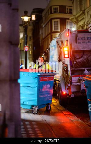 LONDRES - 1 novembre 2020: Bin man déplace une grande poubelle sur le trottoir la nuit Banque D'Images