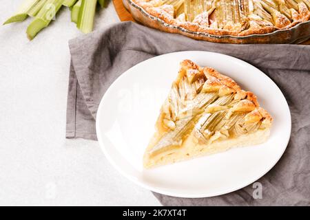 Morceau de tarte à la rhubarbe maison et tiges de rhubarbe sur table blanche. Délicieuse pâtisserie maison Banque D'Images