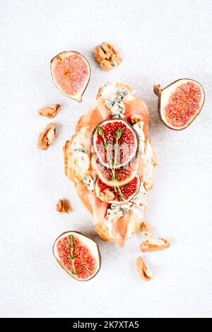 Vue de dessus sur le croissant frais bruschetta avec figues mûres, fromage bleu, prosciutto, noix et herbes sur fond de table en béton blanc. Mise au point sélective Banque D'Images