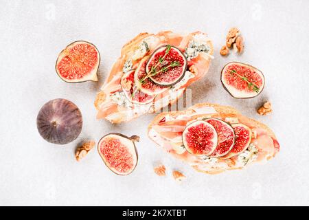 Vue de dessus sur le croissant frais bruschetta avec figues mûres, fromage bleu, prosciutto, noix et herbes sur fond de table en béton blanc. Mise au point sélective Banque D'Images