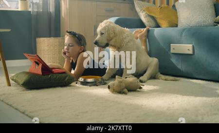 Jeune fille jouant avec le chien avec le jouet et le ballon, assis sur un tapis doux, nourrissant le chiot, parlant et s'amusant avec l'animal de compagnie, passant du temps libre à la maison. Golden Retriever. Banque D'Images