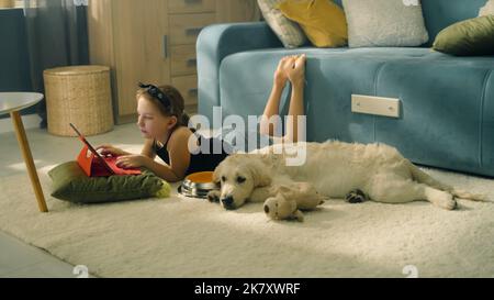 Jeune fille jouant avec le chien avec le jouet et le ballon, assis sur un tapis doux, nourrissant le chiot, parlant et s'amusant avec l'animal de compagnie, passant du temps libre à la maison. Golden Retriever. Banque D'Images