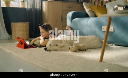 Jeune fille jouant avec le chien avec le jouet et le ballon, assis sur un tapis doux, nourrissant le chiot, parlant et s'amusant avec l'animal de compagnie, passant du temps libre à la maison. Golden Retriever. Banque D'Images