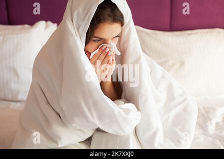 Une jeune femme infectée par un rhume souffle son nez avec un mouchoir Banque D'Images