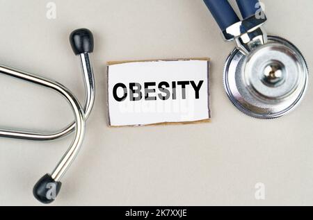 Concept médical. Sur fond gris, un stéthoscope et un panneau en carton avec l'inscription - obésité Banque D'Images