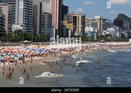 Plage de Leblon, Rio de Janeiro, Brésil. Les gens se bronzent près de la rive avec des parasols colorés. La foule aime nager en mer en été. Voyage tropical Banque D'Images