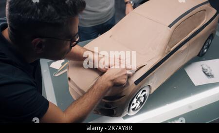 Deux concepteurs automobiles masculins sculptant un modèle futuriste en argile plaline de voiture avec râteau. Conception future de la nouvelle génération de voiture électrique. Travailler dans un studio de conception de voiture moderne. Banque D'Images