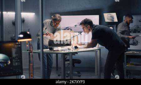 Deux concepteurs automobiles masculins sculptant le modèle futuriste d'argile plaline de voiture électrique avec râteau et d'autres outils. Travailler dans un studio de conception de voiture moderne. Banque D'Images